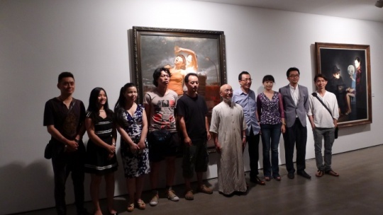 出席現場的嘉賓和部分參展藝術家合影，背景為藝術家馬精虎作品《養(yǎng)蜂人》
