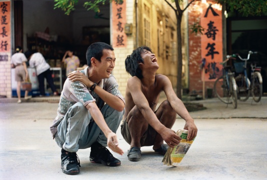 《我和我的老師》鄭國谷（1970-）攝影/錄像/行為 182 × 270 cm  1993 年


1993年，23歲的鄭國谷以《我和我的老師》徹底拋卻過去，登上了他20余年如一日的年輕藝術(shù)之途，至今仍不見盡頭?！拔业睦蠋煛笔青崌仍诩亦l(xiāng)陽江街上偶然遇見的一位瘋子，一無所有，卻無比自由。鄭國谷讀到他不按常理出牌的衣食住行方式背后的顛覆性提問，他說自己雖然蹲下來和“我的老師”一起大笑，但還是“沒他放得開，略顯拘謹(jǐn)”。然而，非常規(guī)能量已經(jīng)接續(xù)，鄭國谷之后20年如一日的持續(xù)性“無法不破，不立一法”的藝術(shù)實踐不斷積淀著作品的厚度：他是最早一批進(jìn)行實驗攝影的藝術(shù)家之一，那些由傻瓜相機(jī)拍攝的《度蜜月》的作品被很多藝術(shù)家所深深銘記；2001年，他購買了七套頂層商品房，打通連接建成自己的家，在房地產(chǎn)市場崛起之前已經(jīng)在發(fā)問；他推動成立的陽江組致力于對傳統(tǒng)書法破綻的尋找，并關(guān)注到向來被忽視的底層書寫；他按照先鋒藝術(shù)家的生活方式將教學(xué)帶到酒吧，給每位學(xué)生打99分；他建于郊區(qū)的3萬平米個人當(dāng)代藝術(shù)實驗田則經(jīng)歷了從天馬行空、漫無邊界的“帝國”到“了園”的不同階段，耗近十年之功而至今未了，土地制度、人權(quán)、資本、想象力、藝術(shù)的邊界等等均攪和在一起……很少有藝術(shù)家像鄭國谷那樣將自己的生活和藝術(shù)的先鋒實驗像如此緊密而多樣地交織在一起。這位受到多方重視的藝術(shù)家既是海內(nèi)外的重要大展的?？?，卻又始終沒有離開自己出生的小城陽江，吃酒喝茶關(guān)照家人，并把身邊的生活重又變成藝術(shù)。
