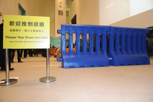 關(guān)尚智的作品《水馬》茅臺與水以1：999的比例注入藍色裝置之中，在展覽大廳的入口處，擺放著熱情的提示語：歡迎推倒這墻