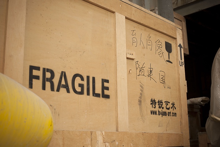 在疊放的木箱之中，被物流工人隨意寫上的用以標識內(nèi)部作品內(nèi)容的七個漢字中有兩個是錯別字。
